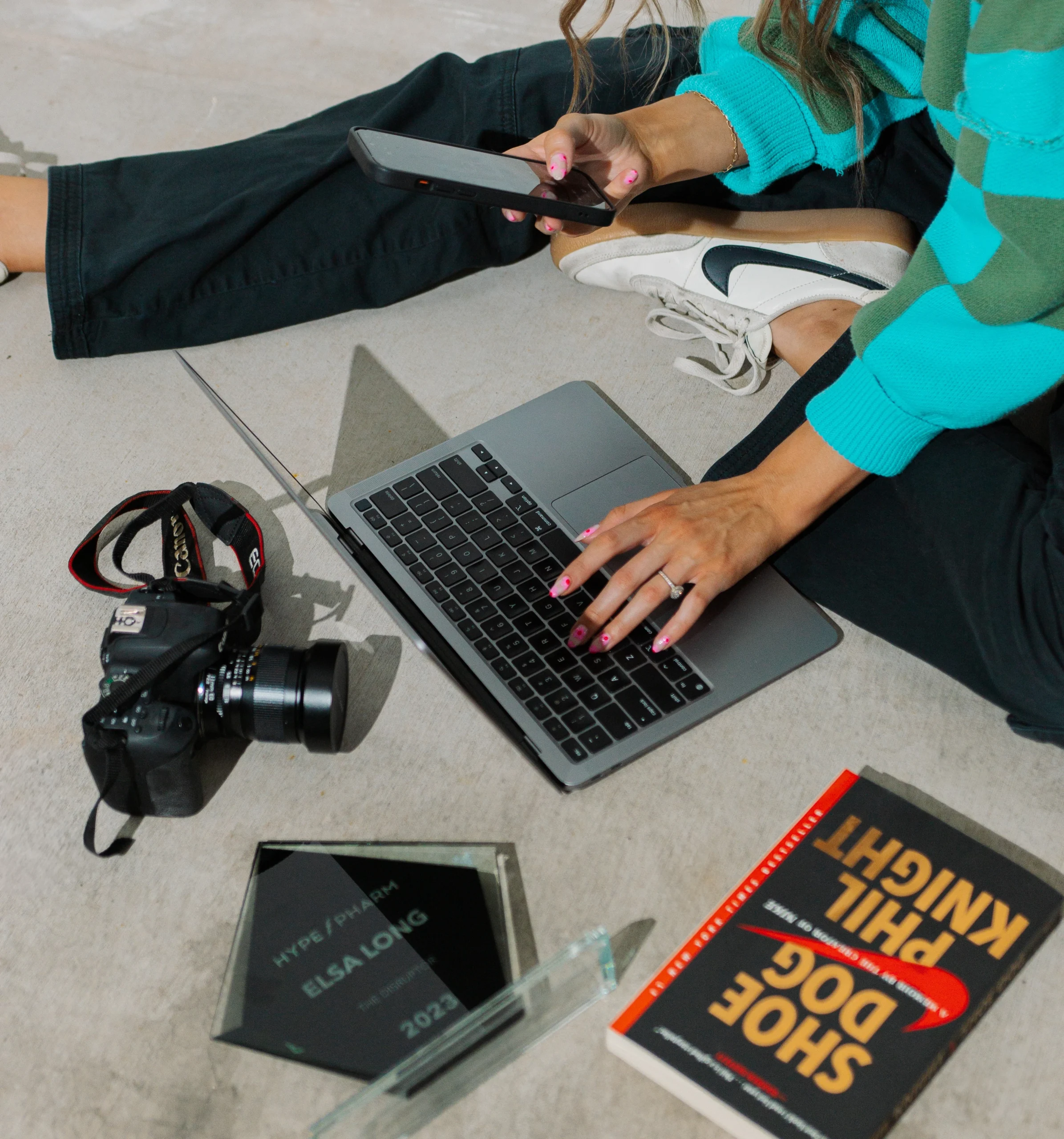 Elsa Long working creatively with a laptop, camera, phone, and design award